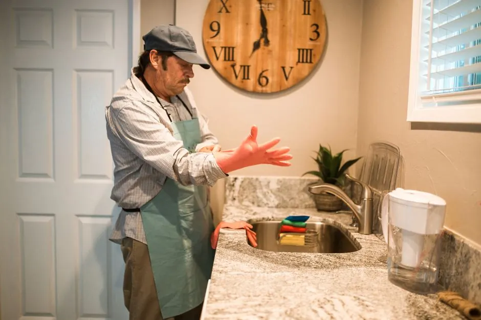 A senior man prepares to clean a kitchen sink wearing rubber gloves.
